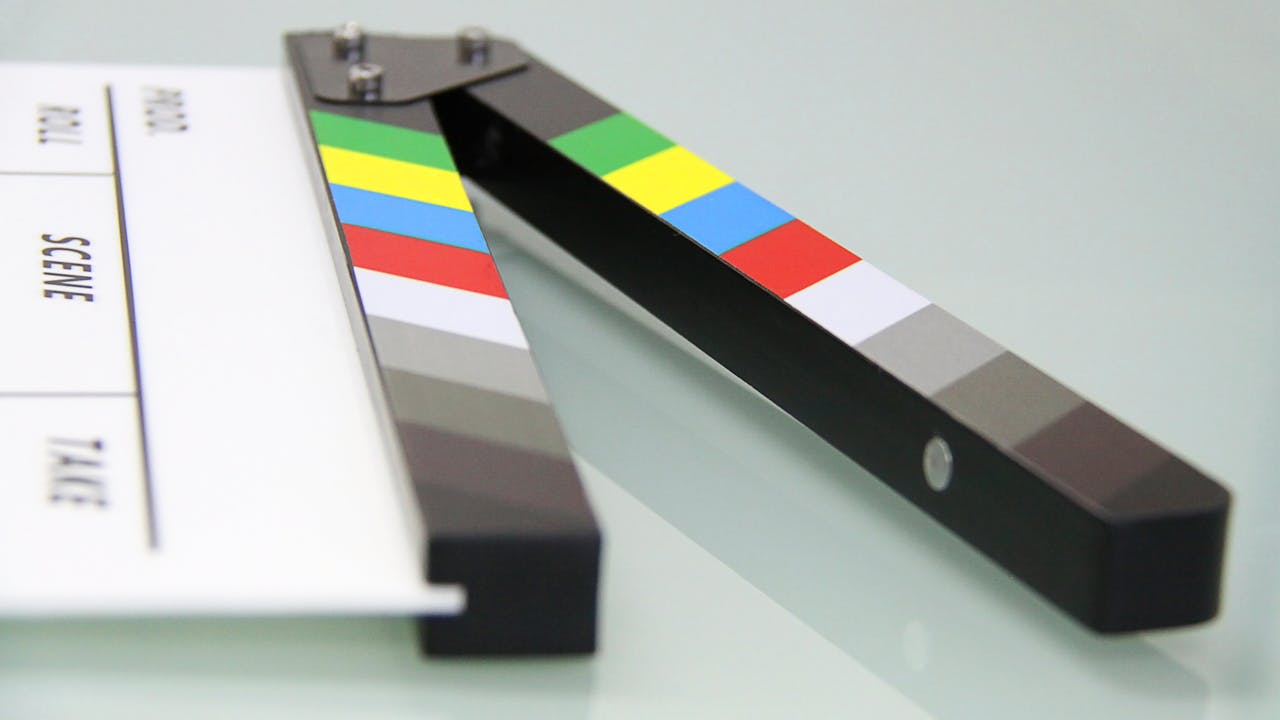 hero-img-01 Colorful clapper board on a white surface, used in filmmaking. Ideal for entertainment and movie themes.